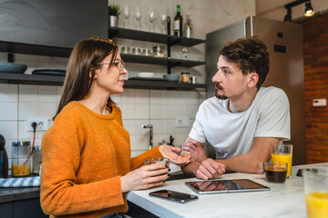 Two people young couple adult man and woman husband and wife or boyfriend with girlfriend in the kitchen in the morning with coffee and juice talking and chat daily routine real people