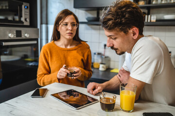 Two people young couple adult man and woman husband and wife or boyfriend with girlfriend in the kitchen in the morning with coffee juice mobile phone and digital tablet talking and chat daily routine