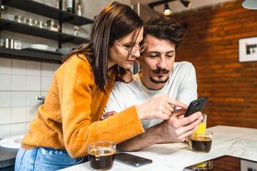 Two people young couple adult man and woman husband and wife or boyfriend with girlfriend in the kitchen in the morning with coffee juice mobile phone and digital tablet talking and chat daily routine
