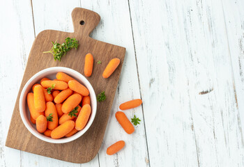 Baby carrots in a bowl over wooden table with herbs and copy space © Odu Mazza