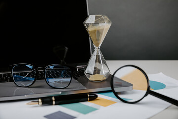 Hourglass, laptop and charts close-up, business and time management concept