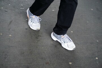 Junger Mann mit grau-weißen Turnschuhen und schwarzer Jeans läuft auf Straße 