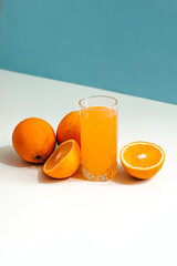Fresh juice with ripe oranges in a glass on a white and blue background. Oranges cut into slices. Vitamin juice, a healthy lifestyle. Vegetarianism, vegan, diet, fruit, nectar. Homemade juice, drink.