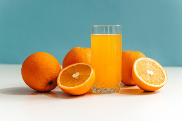 Fresh juice with ripe oranges in a glass on a white and blue background. Oranges cut into slices. Vitamin juice, a healthy lifestyle. Vegetarianism, vegan, diet, fruit, nectar. Homemade juice, drink.