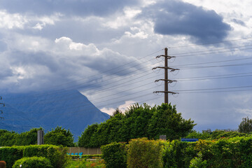 Power lines, high electric pole at the foot of a mountain forest in the Swiss Alps, rain clouds...