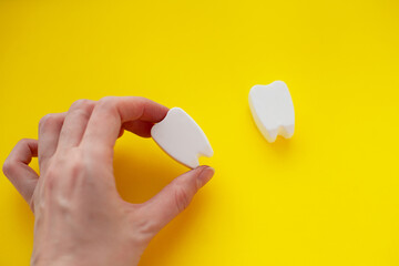 Fototapeta na wymiar Hand holding white plastic teeth shapes isolated on yellow background, representing dental care concept, teeth alignment with braces abstract.