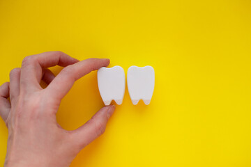 Hand holding white plastic teeth shapes isolated on yellow background, representing dental care...