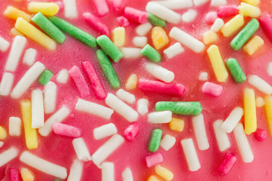Bright colorful sprinkle sugar background, pink glazed donut texture close-up