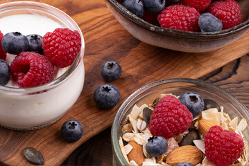 Healthy breakfast with yogurt and raspberries, blueberries, homemade muesli with nuts, on a wooden rustic table