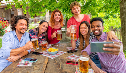 happy multiratial group of friends making a celebratory toast with wine on a picnic table outdoor in the terrace. people gathering in summer happy hour laughing in a party. joy and lifestyle concept