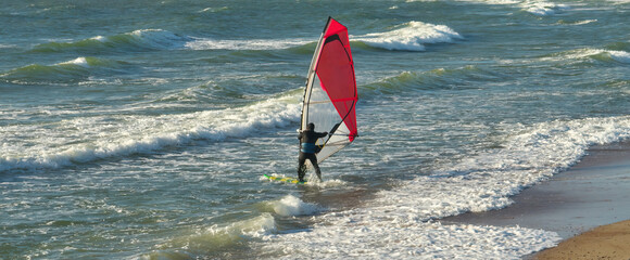 Windsurfer sailing and catching the wind. A male athlete is fond of windsurfing. He moves on a...