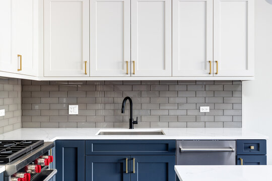 Detail shot of a kitchen with blue and white cabinets,  black faucet, and a subway tile backsplash.