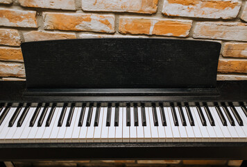 A modern expensive black piano, a musical instrument close-up stands against a brick wall in the...