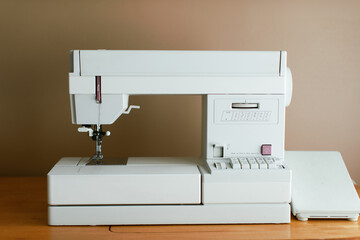White simple sewing machine set up at a home office desk.