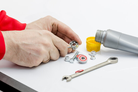 Mester applies lubricant with a screwdriver and stuffs the bearing. On the table are a tube, a wrench and bearings on a white background