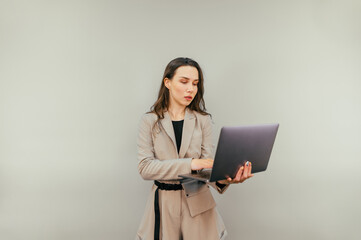 Business woman in a beige suit opens a laptop to work with a serious face on a beige background. Attractive woman working on laptop, isolated.