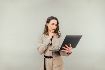 Portrait of a pensive business woman in a beige suit with a laptop in his hands stands on a beige background and looks at the camera with a pensive face.