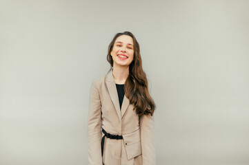 Portrait of a joyful woman with braces on her teeth emotionally smiling on a beige background and looking at the camera, wearing a beige jacket