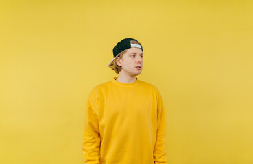 Handsome man in cap and yellow sweatshirt isolated on yellow background and looks away with a serious face.
