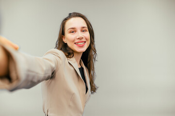 Happy woman in jacket making selfie on beige background with smile on face looking at camera in smartphone. Isolated