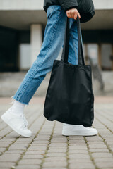 Close photo of female legs in sneakers with a bag in hand on a walk.