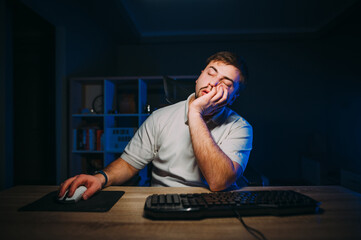 A tired man in a white T-shirt fell asleep while working at home on the computer at night.