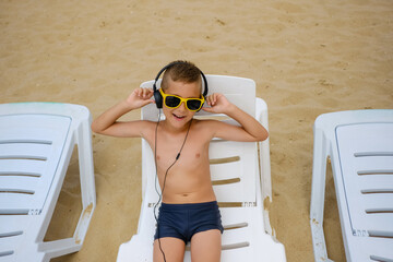 Young boy in sunglasses listens to music with headphones on the sea beach.