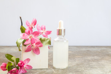 Cosmetic glass transparent bottle with dropper for hyaluronic acid. Square podium and pink cherry blossoms on a white background. bottle mockup