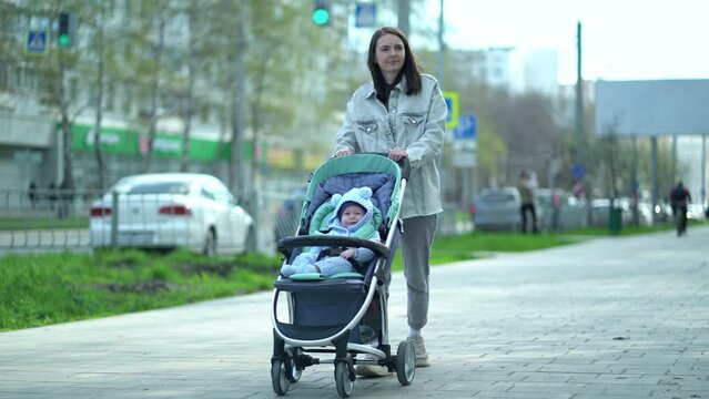 Woman walks with baby stroller in which child boy is sitting