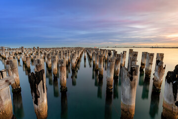 The remaining timber pylons of the historic Princes Pier in Melbourne Australia with calm water reflecting the sunset colors in the clouds.