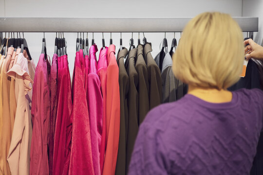 A woman looks at clothes hanging on hangers in a fashion store. Shopping. Selective focus.