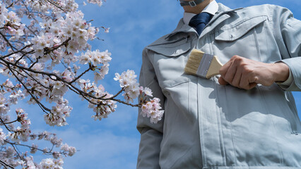 ハケを持った作業服の男性と桜｜建設業・塗装業　入社イメージ