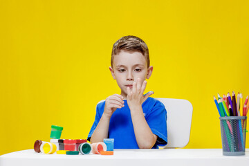 A little preschooler sits at a table, holding a brush in his hand and painting paints his palm. Preschooler development.