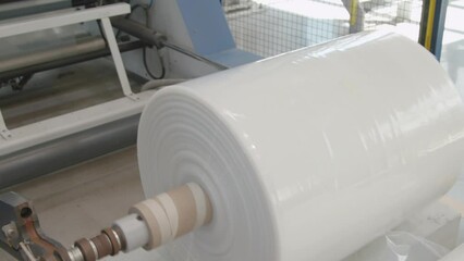 Large film roll released from multilayer blown film extrusion machine. Flexible packaging and film processing, chemical industry production line. Industrial plastic usage themes.