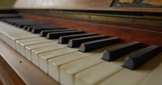 Close up shot of the keyboard of an old vintage piano. Camera moves backwards revealing more of the piano.