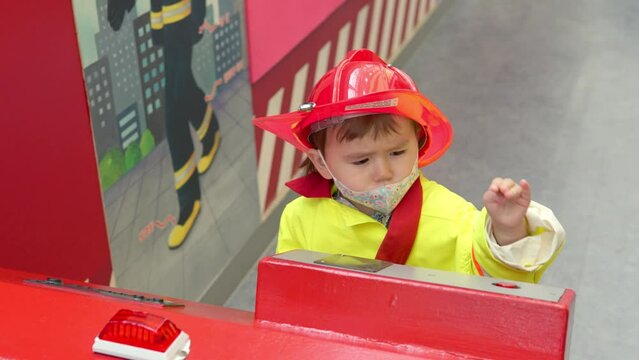 Adorable Korean-Ukrainian multi-ethnic toddler pretending to be a firefighter with a bright red safety helmet and uniform