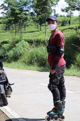 an Asian man in red who was learning to use roller skates on a concrete road with a panoramic view...