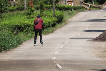 an Asian man in red who was learning to use roller skates on a concrete road with a panoramic view of a fresh green tea plantation. Commemorating World Skate Day
