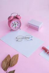 Product Presentation of Minimalist Concept Idea. square glasses, gift box, clock and dry leaves on pink paper background.