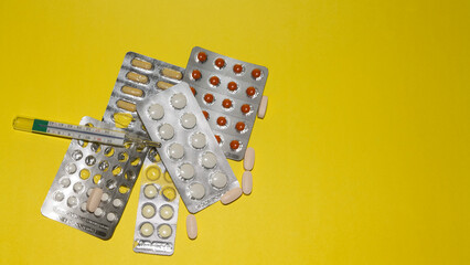 Different medicines in tablets, medical mercury thermometer on yellow. High-quality photo