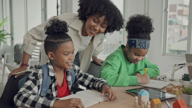 African American female teacher standing with pupils teaching writing lesson in modern classroom.