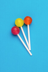 Three colorful lollipops on sticks on a blue background. Minimal concept. Sweet candies.