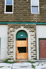 An abandoned old building and broken door way with plywood boarding it up.