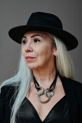 Vertical medium close-up studio portrait of beautiful mature woman with long gray hair wearing...