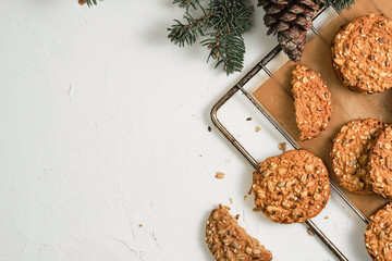 Freshly baked oatmeal biscuits with sunflower seeds are cooling on a tray. Concept of simple homemade baking for the new year or Christmas. Background is decorated with spruce branches, top view