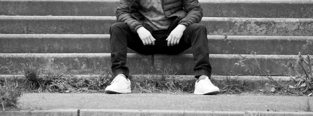 A stylish man is sitting on the stairs in jeans and sneakers