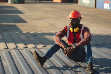 African American male technician or engineer. Sit near a container and look tired and sleepy or unemployed. Logistics industrial cargo mover concept.