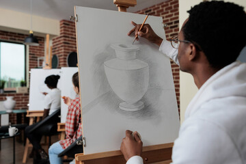 African american student attending art lesson working at creative artwork drawing vase model using...