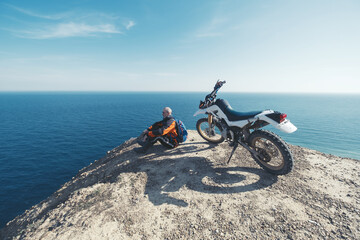 Elderly man resting in enduro motorcycle trip on mountain cliff with amazing sea skyline view