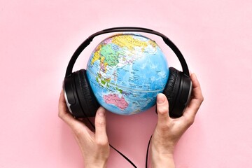 Female hands holding Stereo headphone and a globe on a pink background. World music day concept. Top view. Copy space